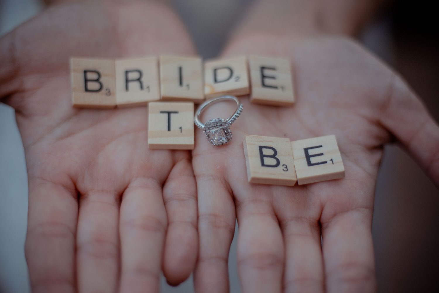 Scrabble tiles spelling out 'BRIDE' held in open palms.