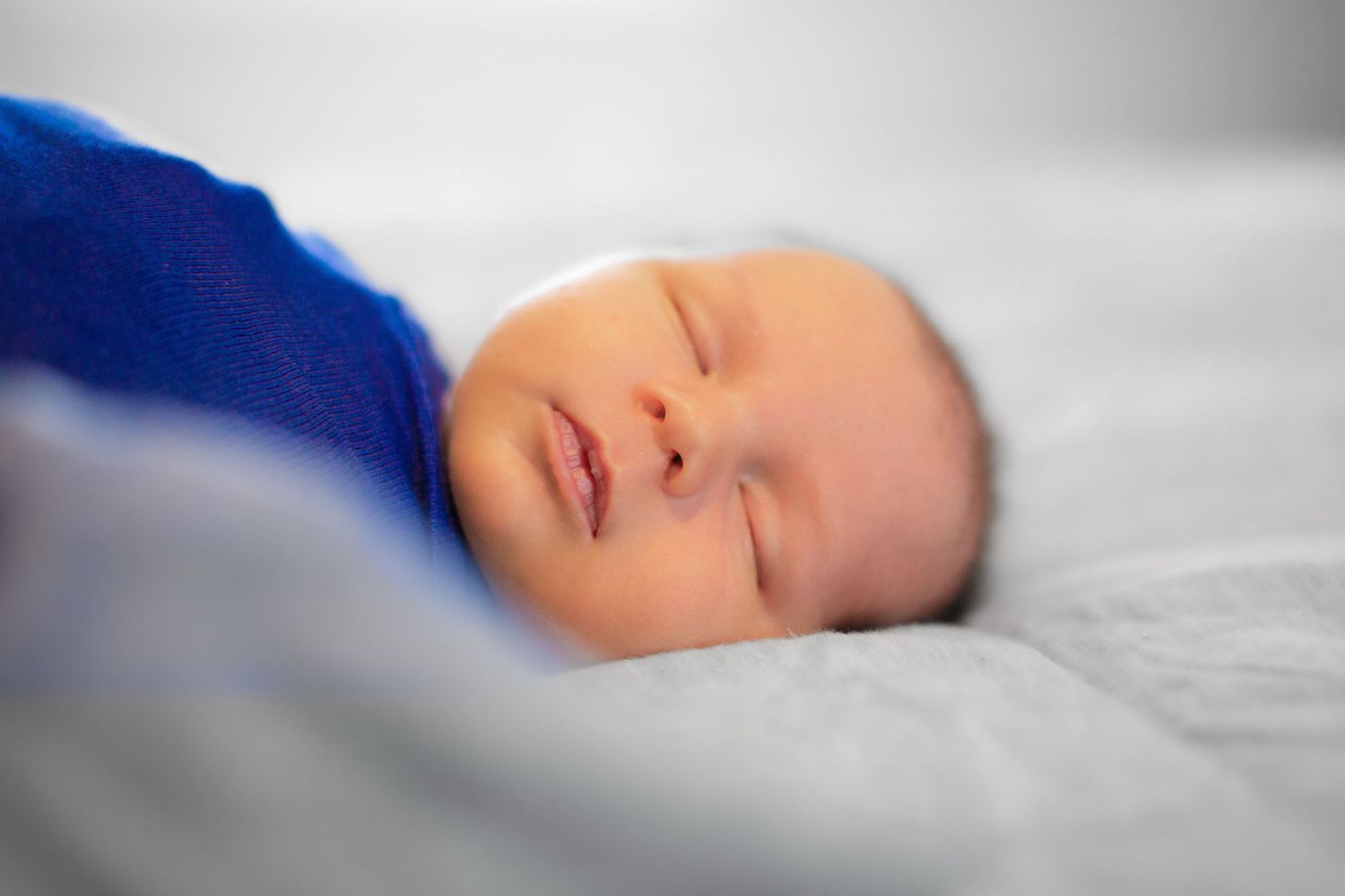 Close-up profile view of a sleeping newborn baby with soft lighting and white background.