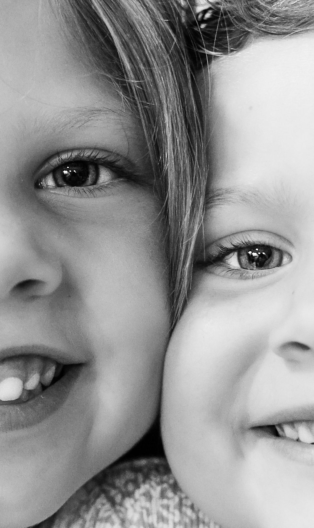 Close-up black and white portrait of two smiling children cheek to cheek with bright eyes.