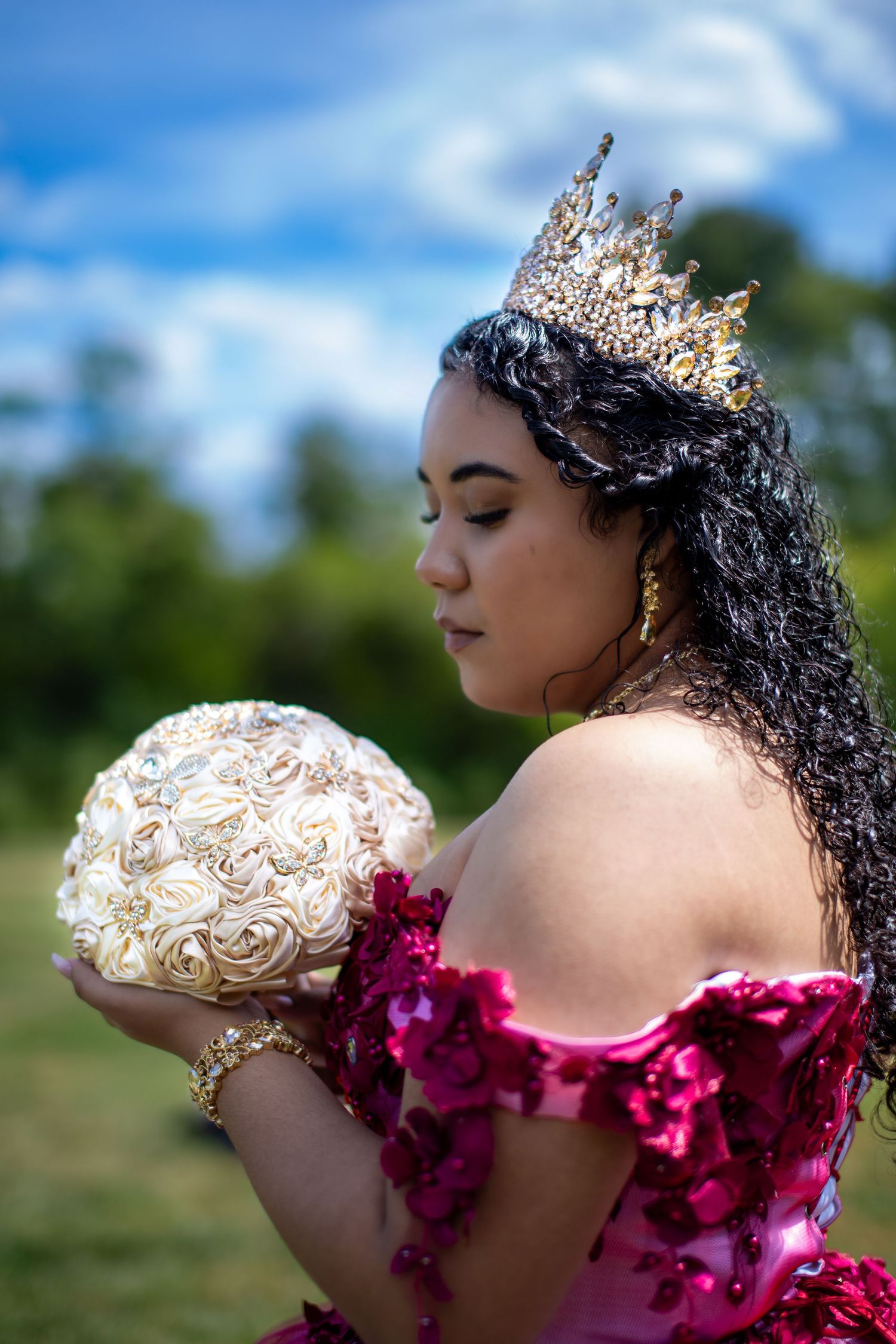 Elegant ballgown with magenta floral details and crown photographed against blue sky.