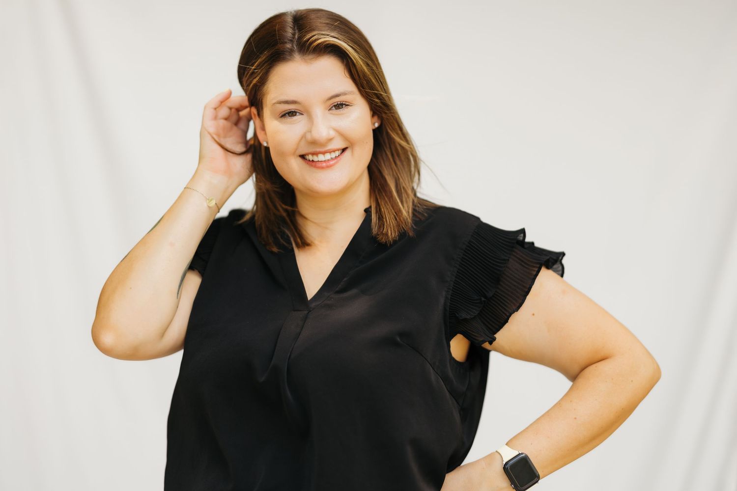 Model wearing black short-sleeve button down top poses against white backdrop with confident smile.