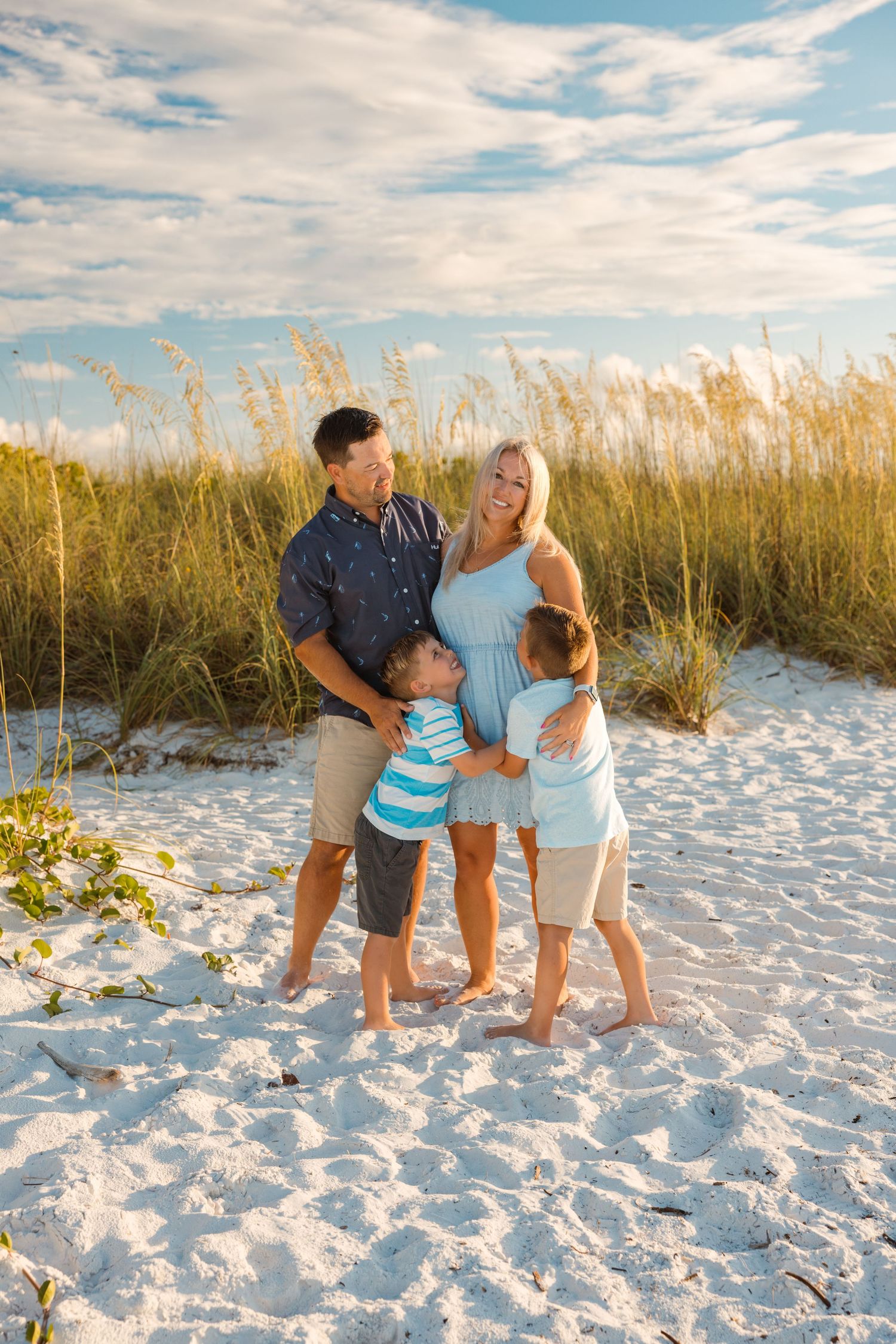 Family enjoying a beautiful evening together on white sandy beach with sea oats and cloudy sky backdrop.