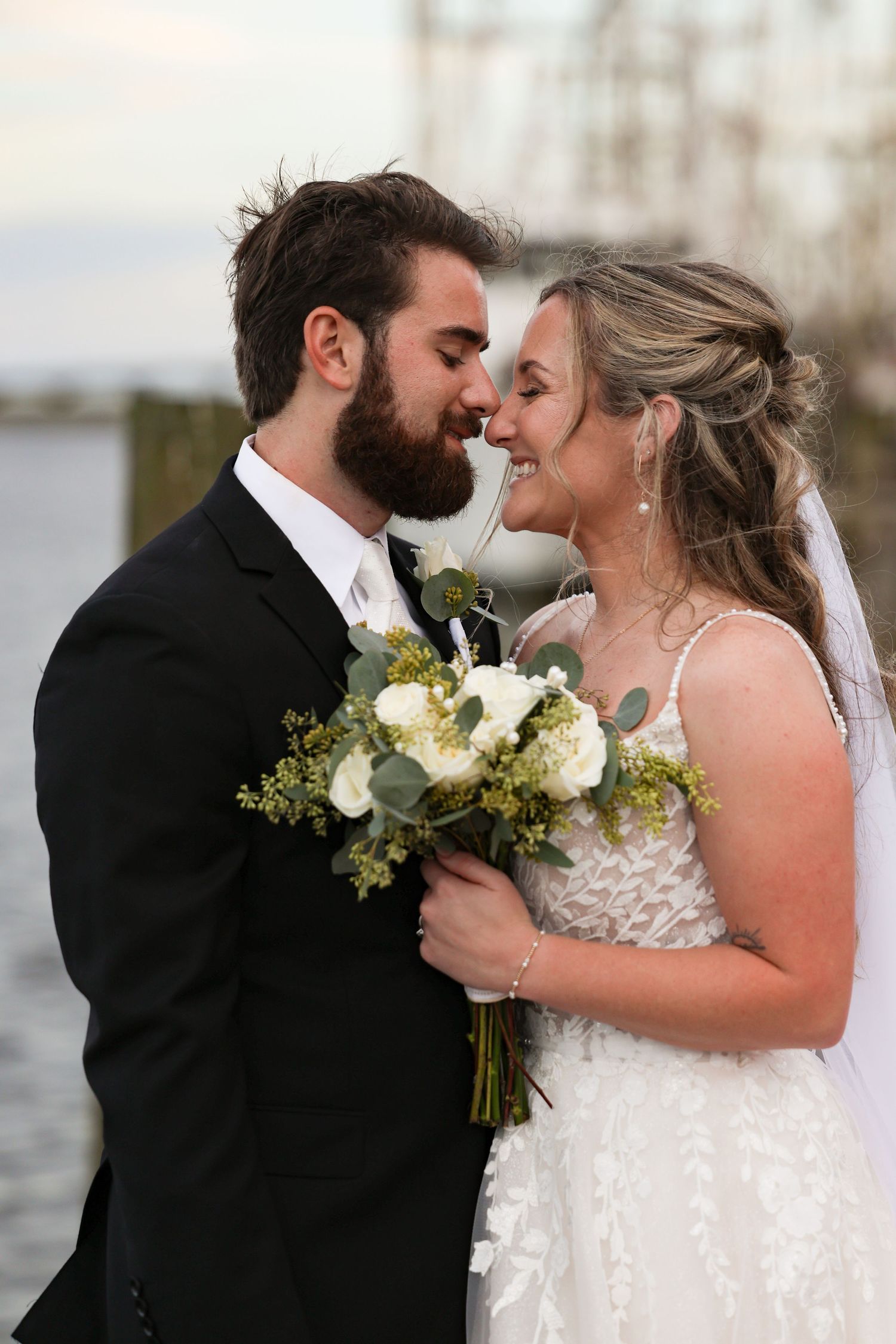 A lovely wedding couple shares an intimate moment with white bouquet against a blurred outdoor background.
