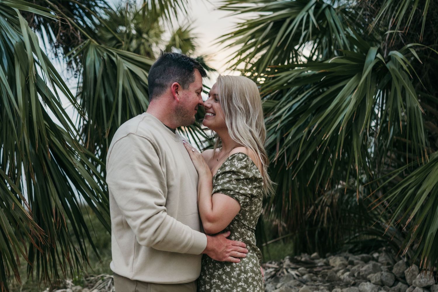 Romantic couple shares intimate moments among tropical palm trees while dressed in neutral beige tones.