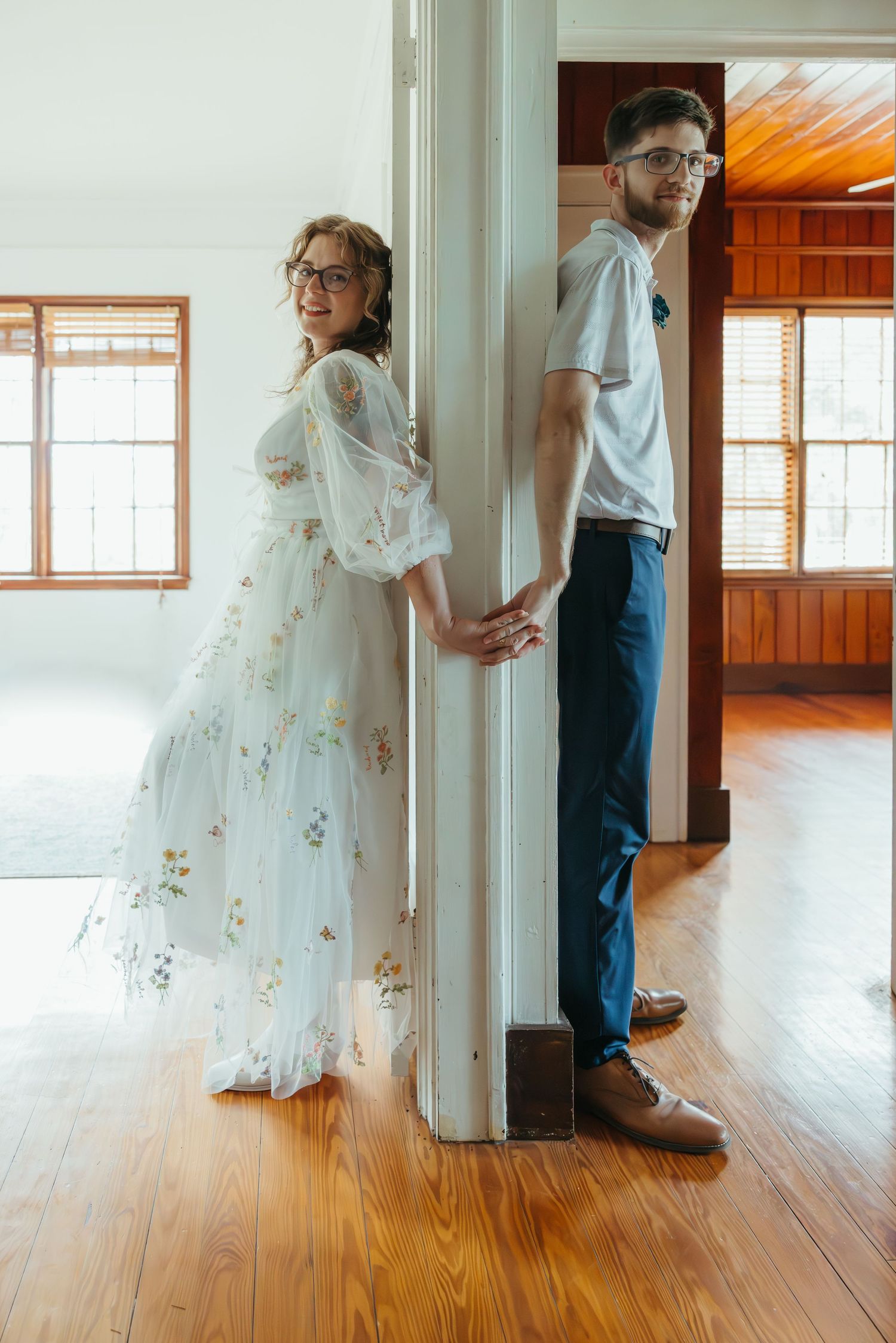A romantic first look moment between a couple where the bride wears a floral embroidered white gown in a sunlit room.