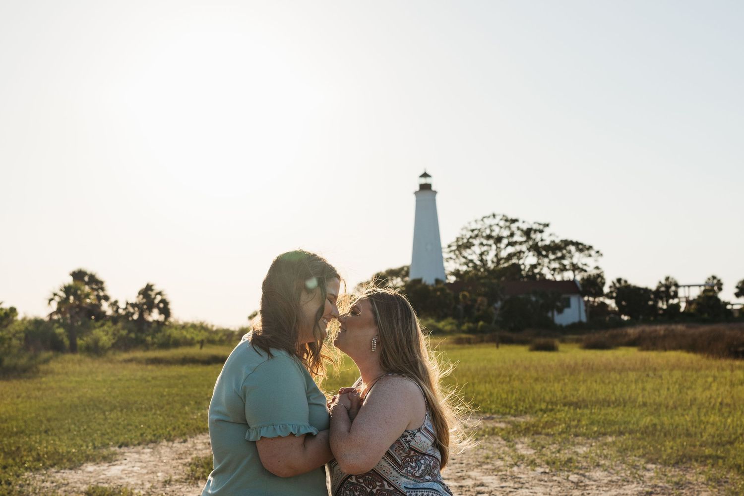 A blissful couple sharing a moment together in front of a white lighthouse during golden hour.