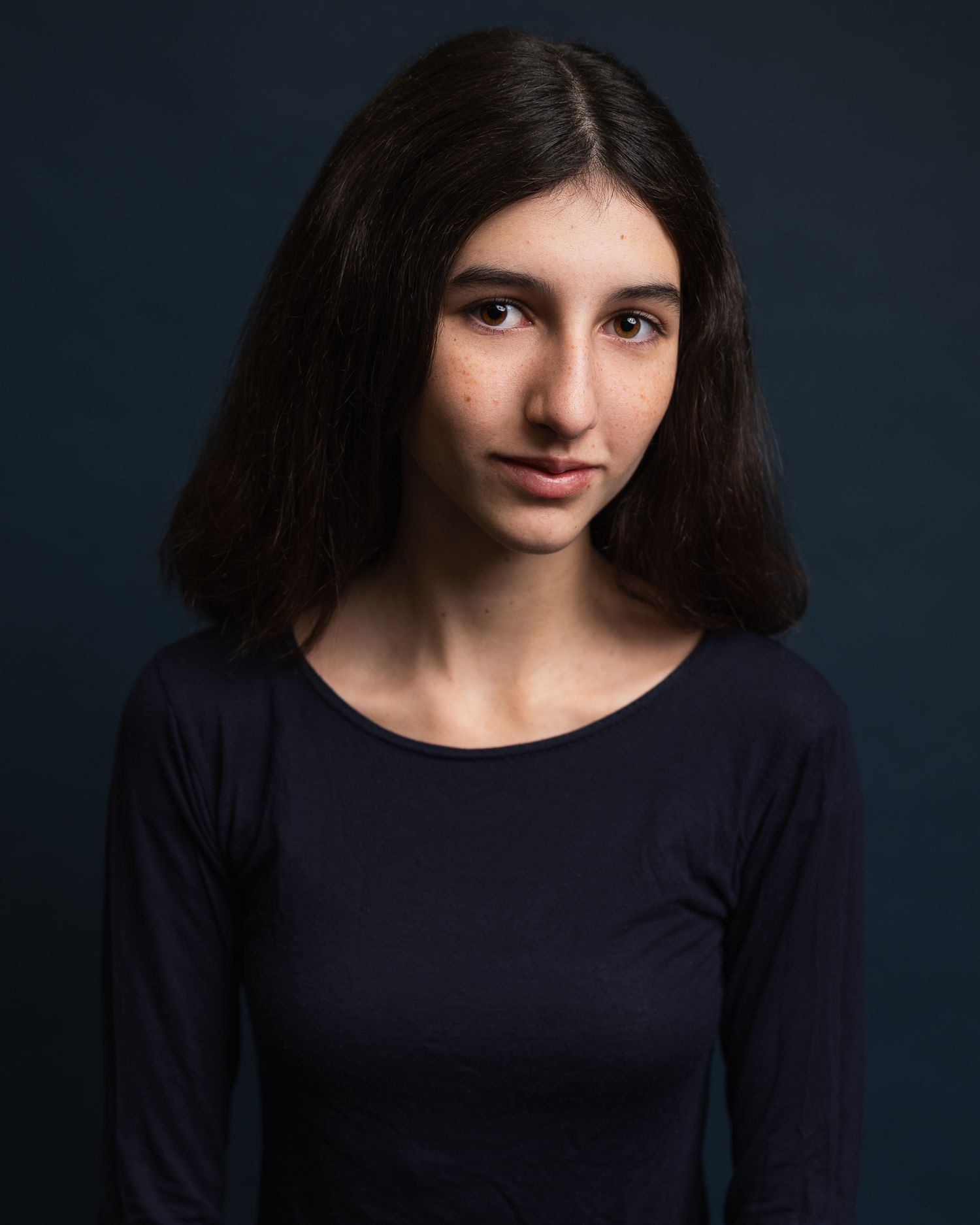 A dramatic portrait of a young woman wearing dark clothes against a navy blue background, Cambridge, UK
