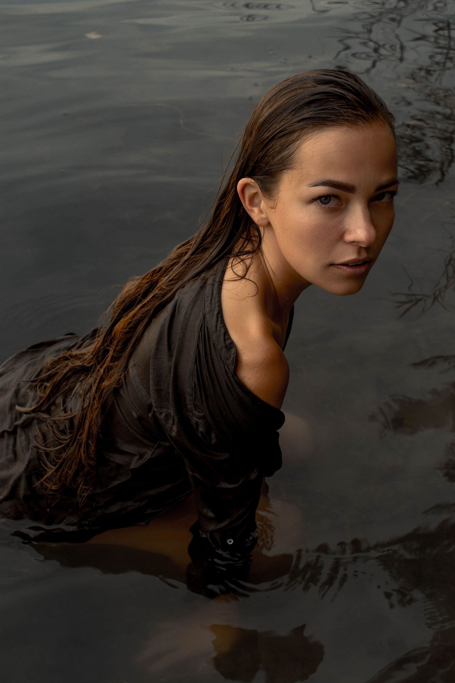 A woman with long dark hair floats in dark water creating a dramatic artistic portrait series. Cambridge, UK