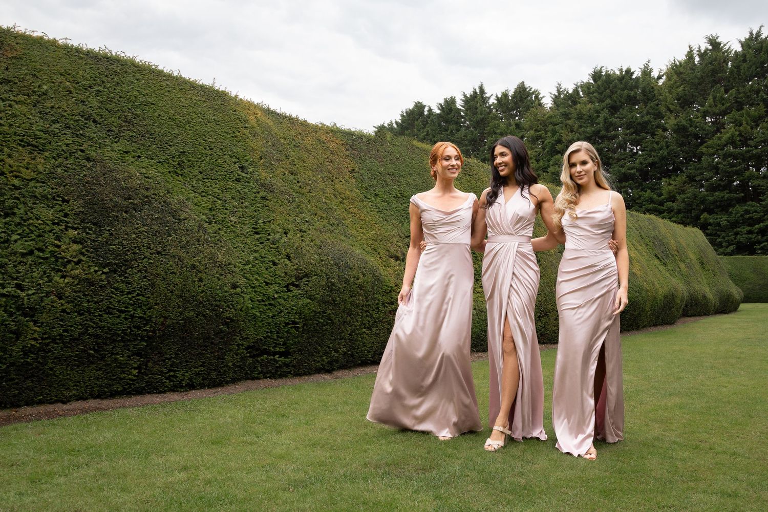 Three ladies in brides mate dresses walks on a grass in the garden in Ely, UK