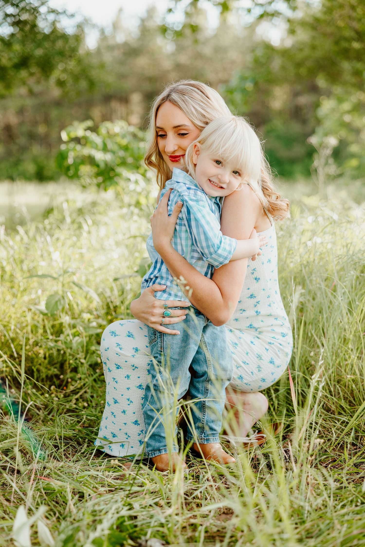 A tender outdoor photoshoot in a meadow setting with soft turquoise and white clothing among tall grasses on a sunny day.