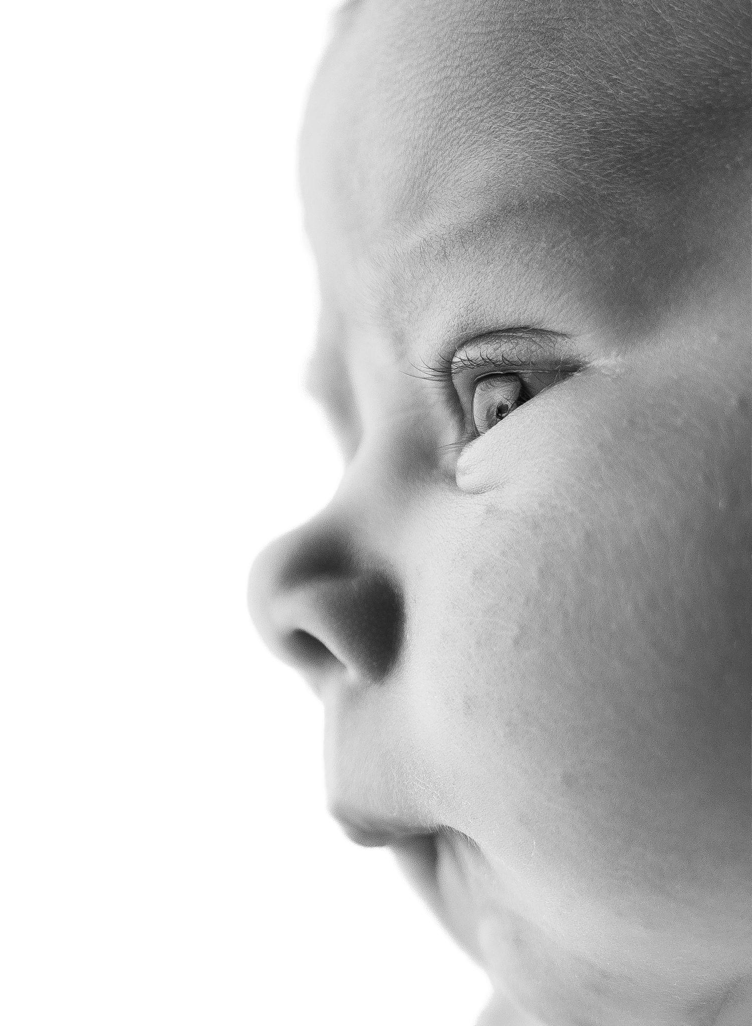 Close-up black and white portrait of a curious baby looking sideways, showcasing delicate features and innocent expression.