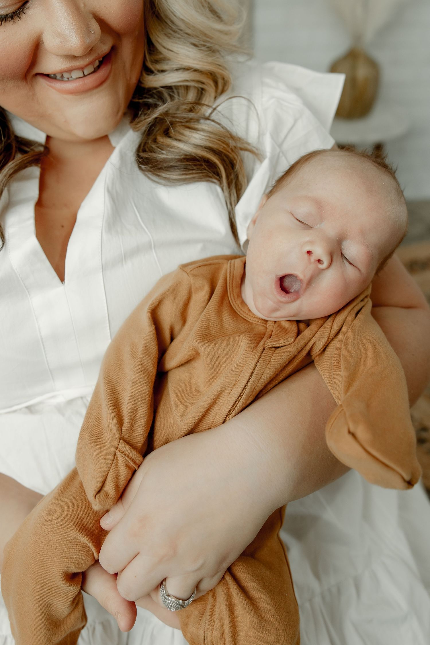 A tiny sleeping newborn baby wearing a brown outfit yawns while being cradled in gentle embrace.