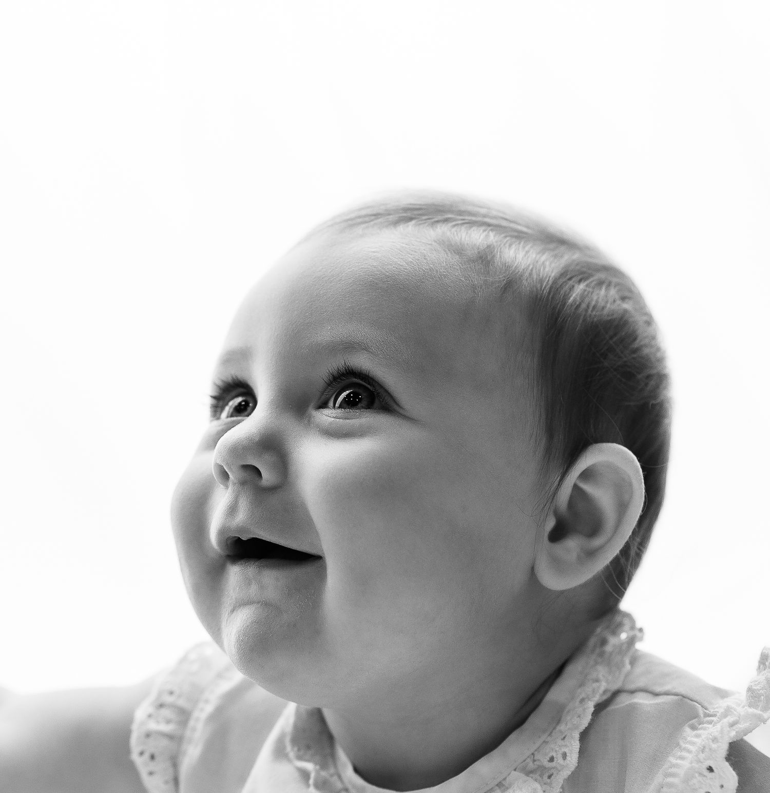 Black and white portrait of a smiling baby looking up with bright eyes and a joyful expression.