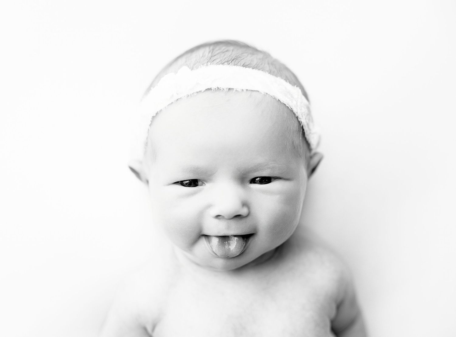 Black and white portrait of a happy baby wearing a white headband against a light background.