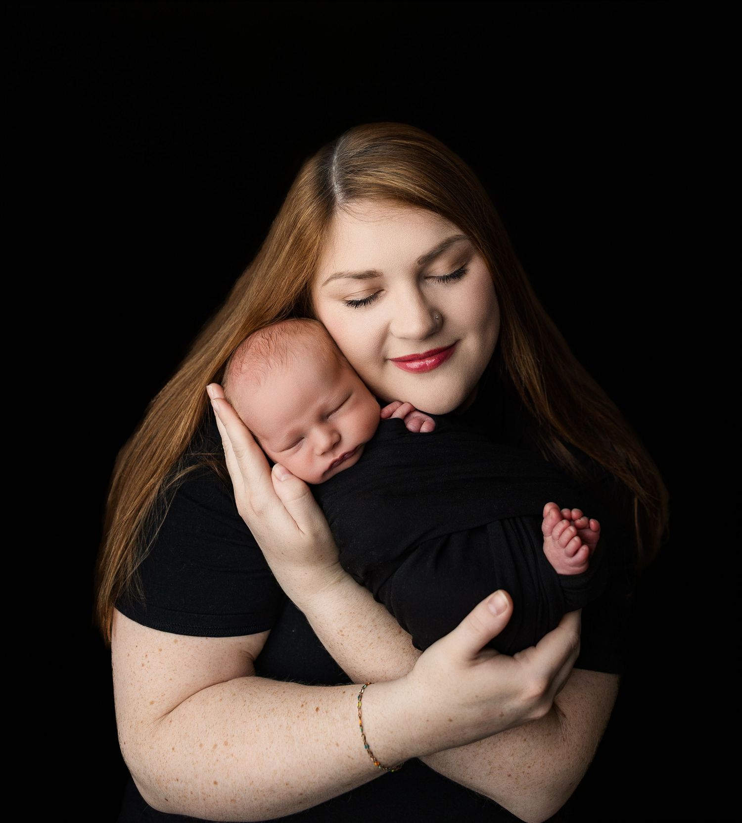 Person in black shirt cuddles and embraces a newborn baby in peaceful intimate portraits.