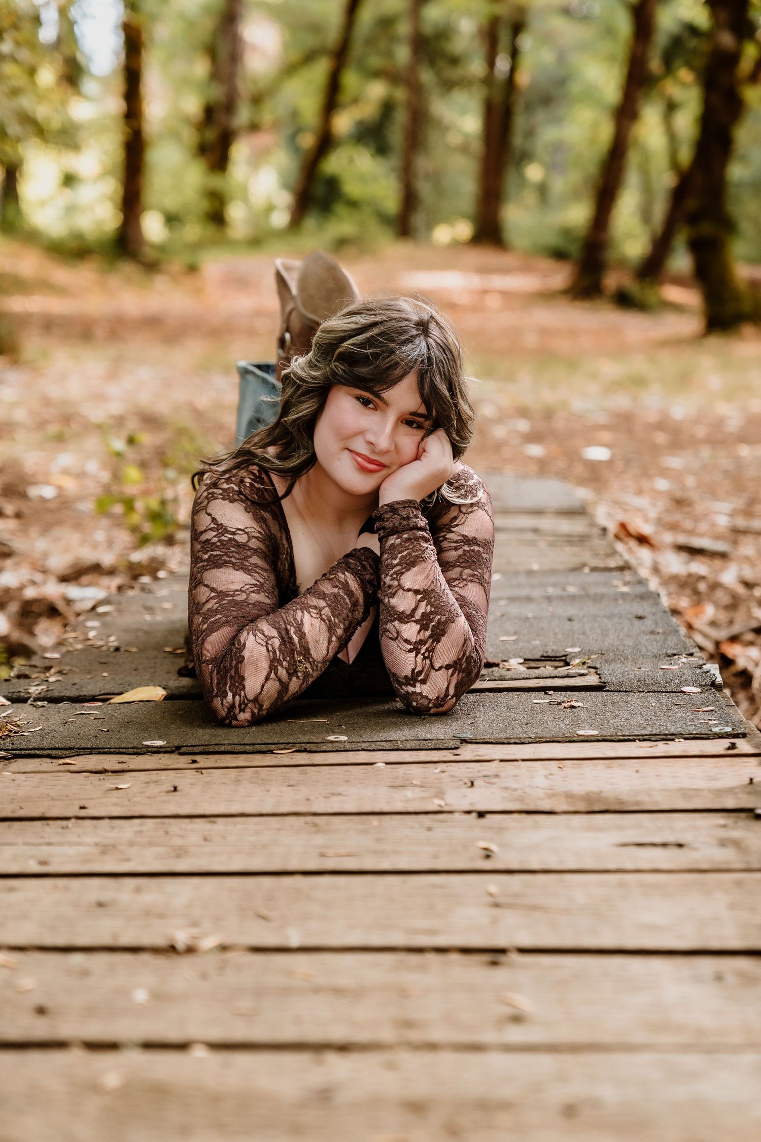 Woman in lace dress lying on wooden deck surrounded by autumn leaves in outdoor portrait session.