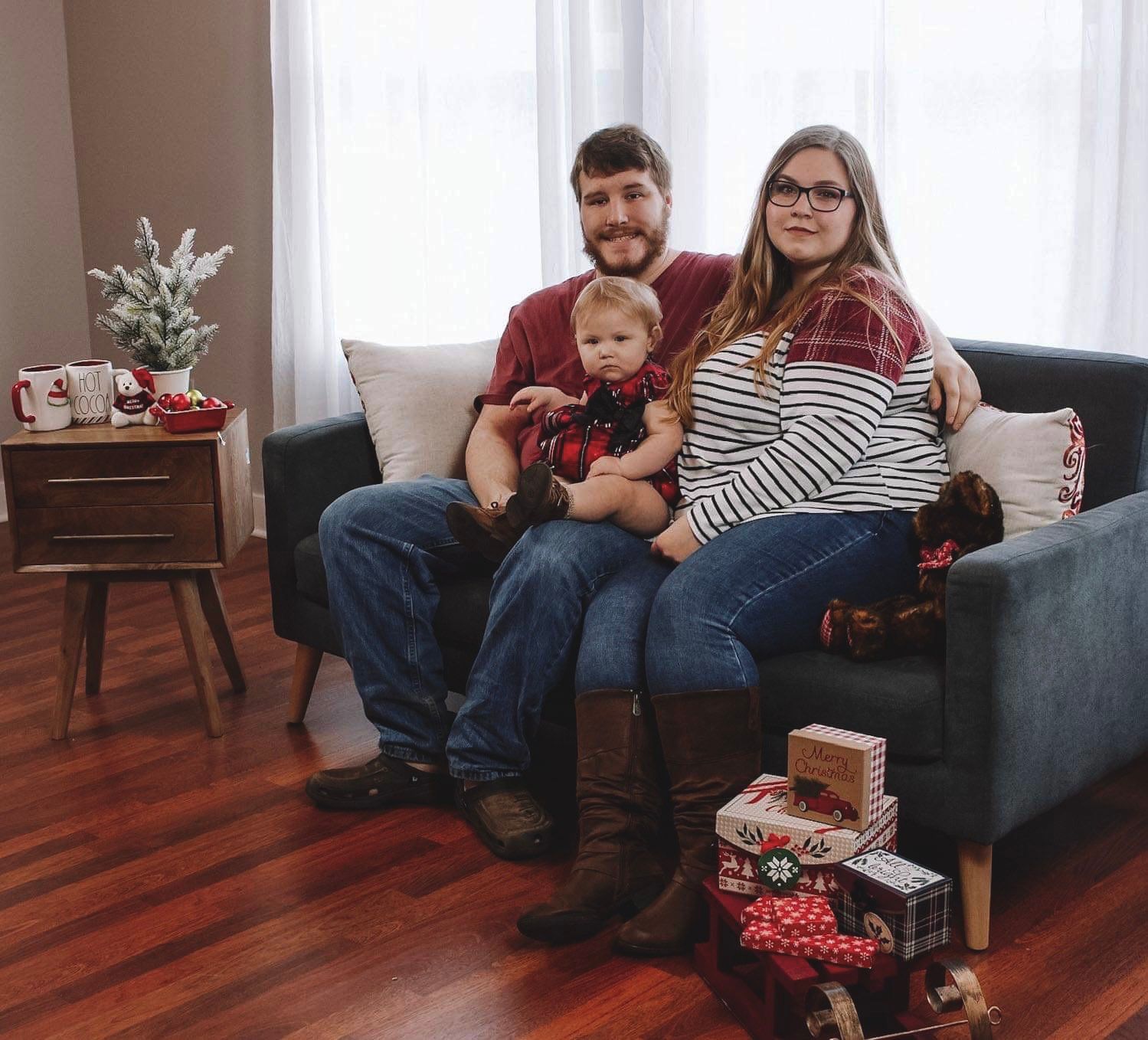 Family relaxing together on couch in living room with hardwood floors during casual photo session.