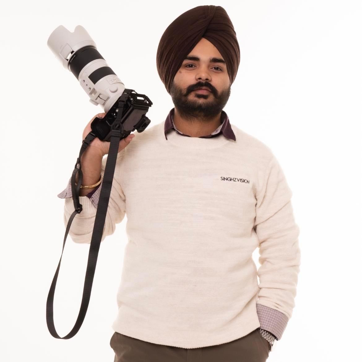 Professional photographer in white sweater displays camera equipment while posing with different lenses.