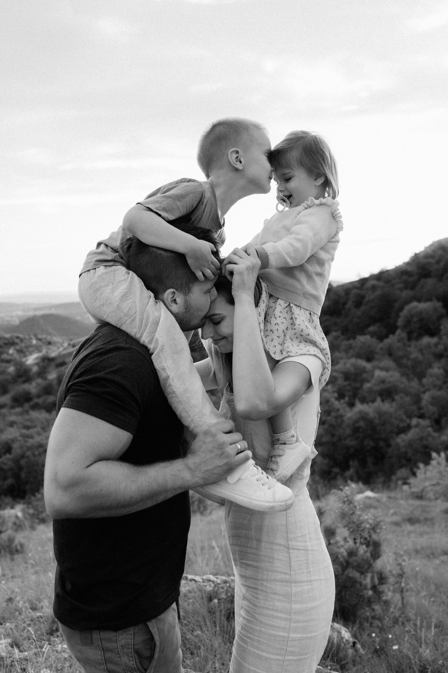 A loving family of four shares a tender moment together outdoors in black and white photography.