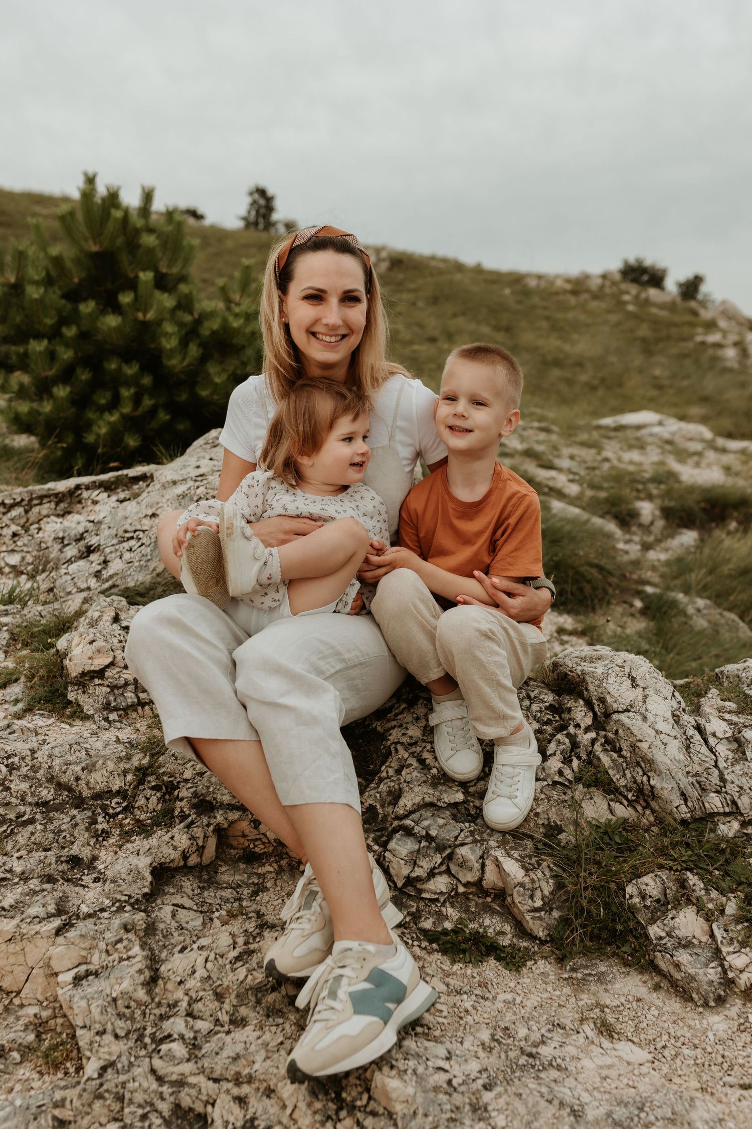 A candid family photo outdoors sitting together on rocky terrain against a cloudy sky.