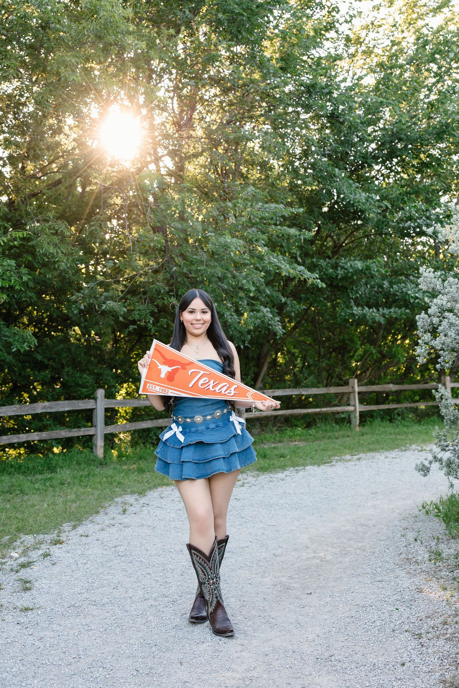 Young woman in denim skirt and cowboy boots holding a University of Texas pennant flag outdoors.