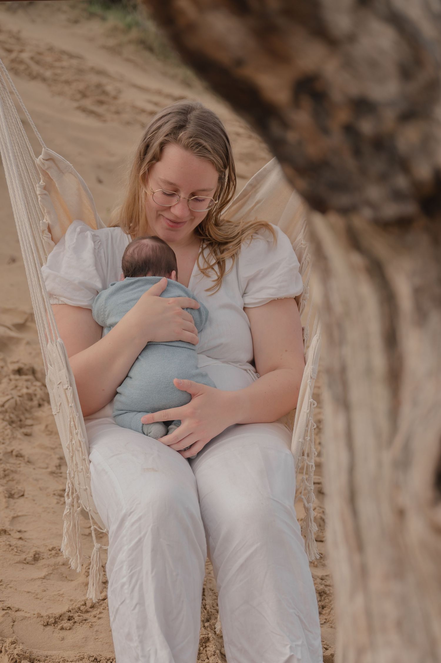 Een teder moment in een hangmat waarin een ouder een slapende baby, gewikkeld in blauw, wiegt tegen een natuurlijke buitenachtergrond.