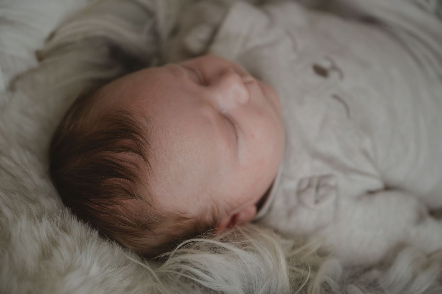 Baby slaapt rustig op zacht wit beddengoed, met donker haar zichtbaar vanuit zijaanzicht.