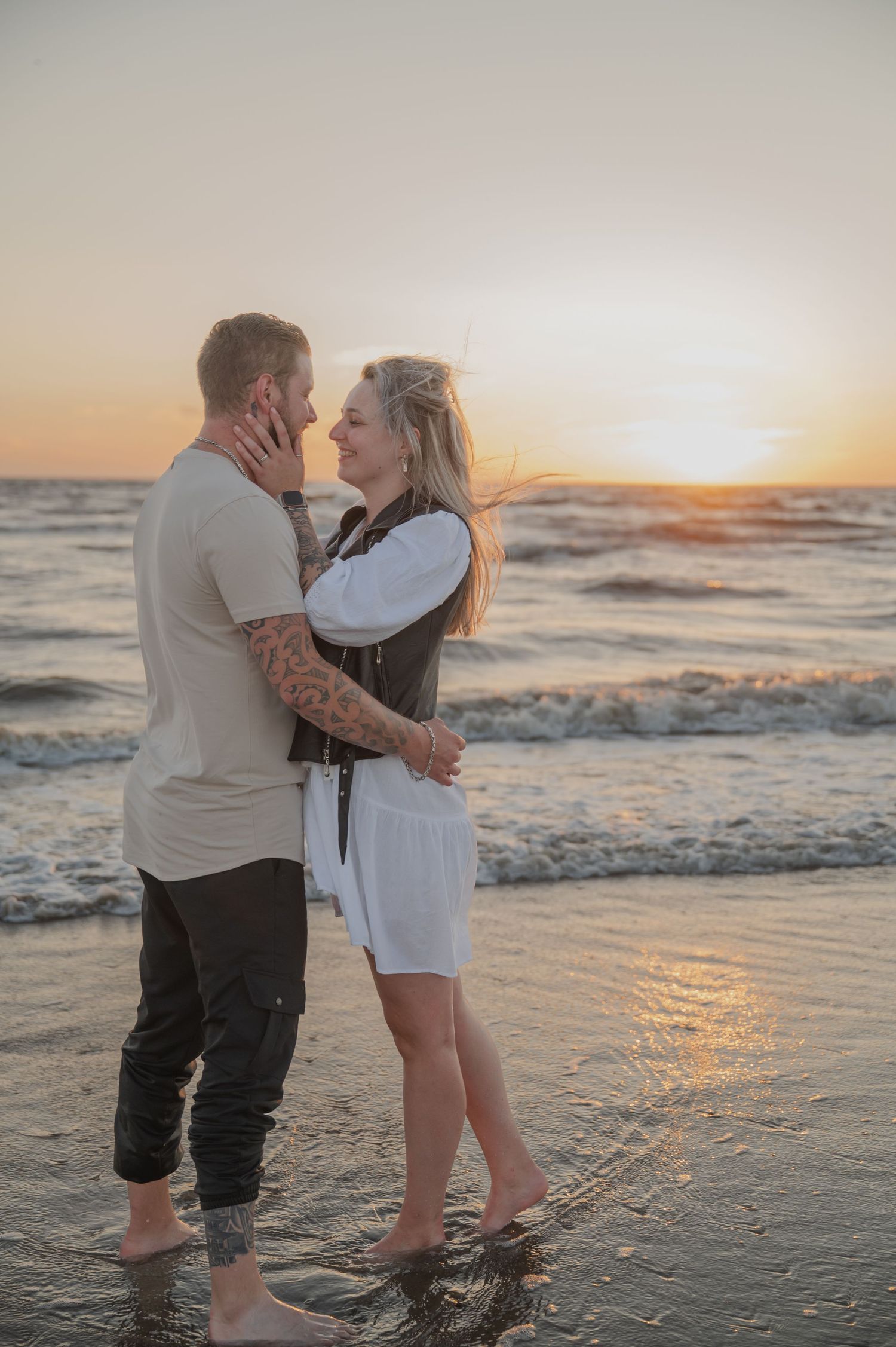 Een romantisch stel omhelst elkaar op het strand bij zonsondergang, terwijl ze in de branding staan met de golven die achter hen aanrollen.