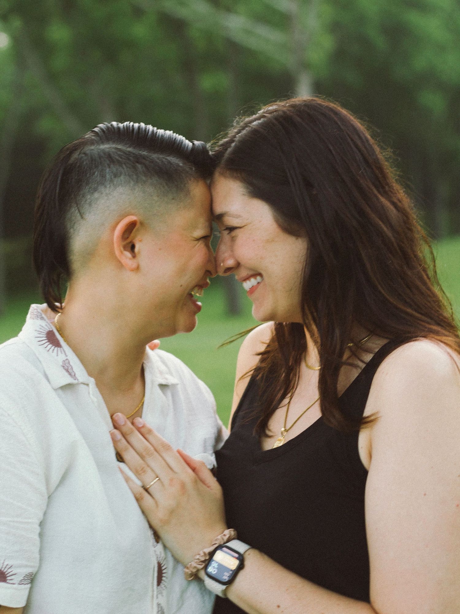 Two women smiling and touching foreheads in an intimate outdoor engagement portrait.