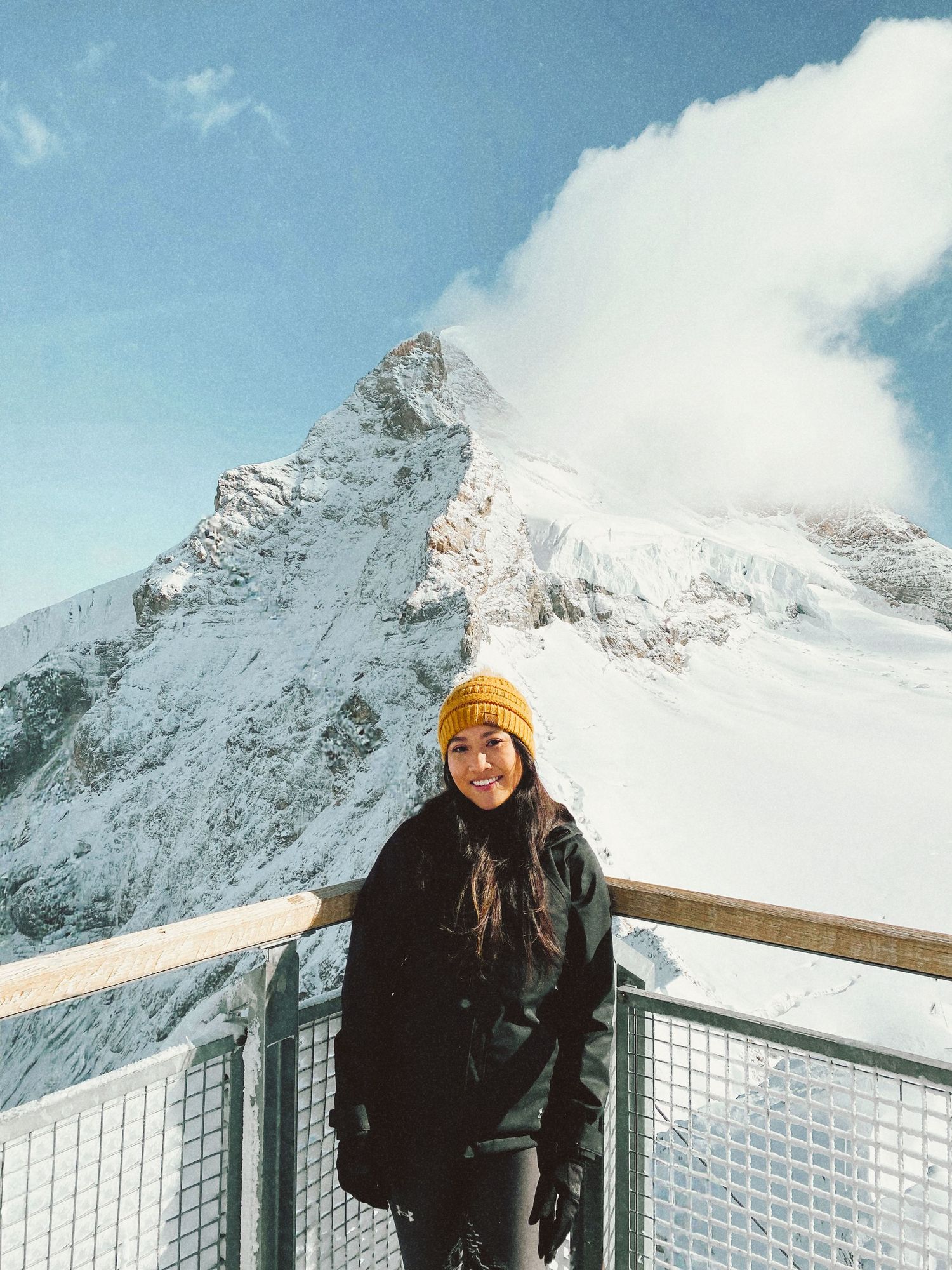 Woman in yellow beanie and black jacket smiling in front of a dramatic snow-covered mountain landscape. Vy Brady, DMV Photographer