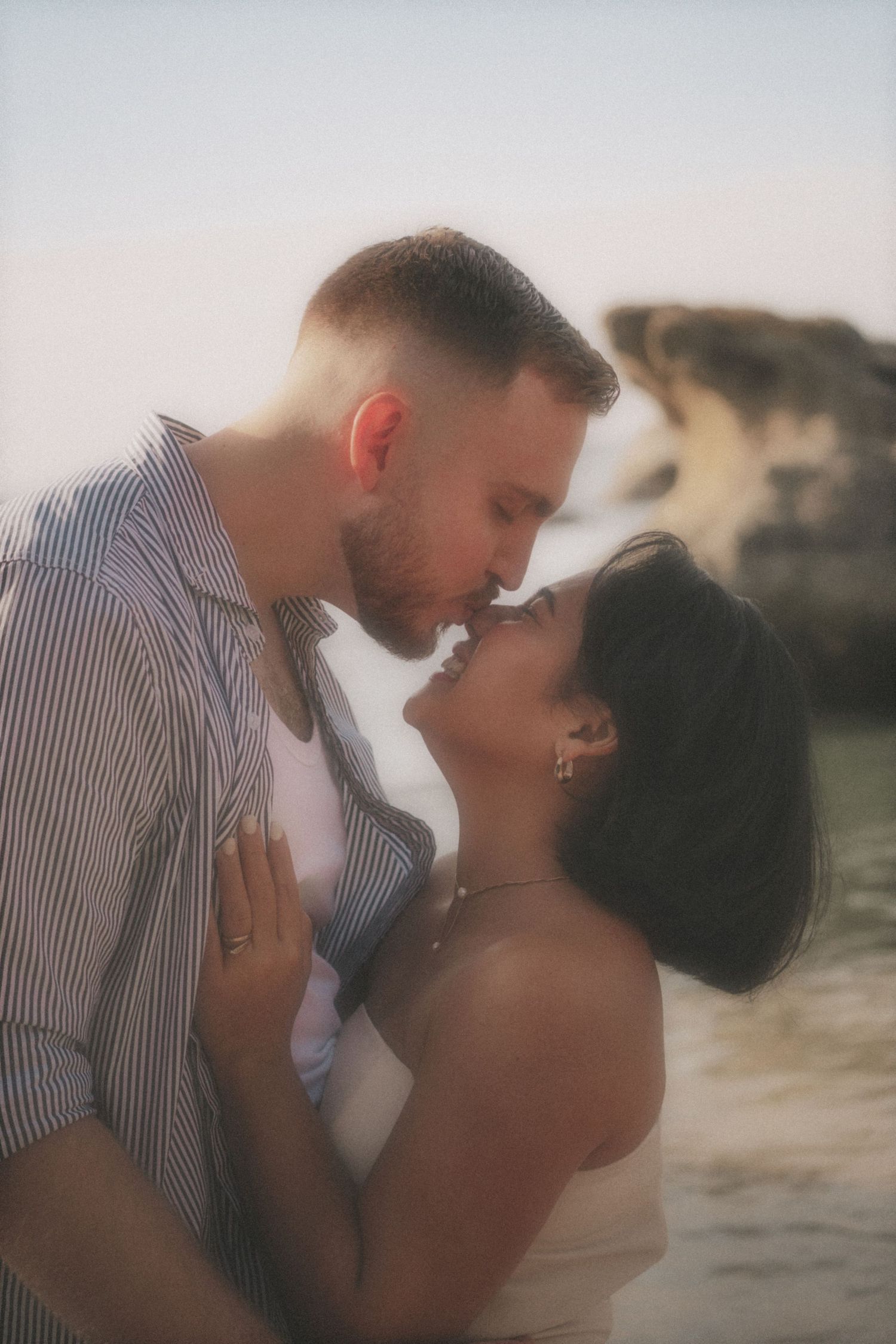 Couple about to kiss, noses touching, at the water's edge among the rocks