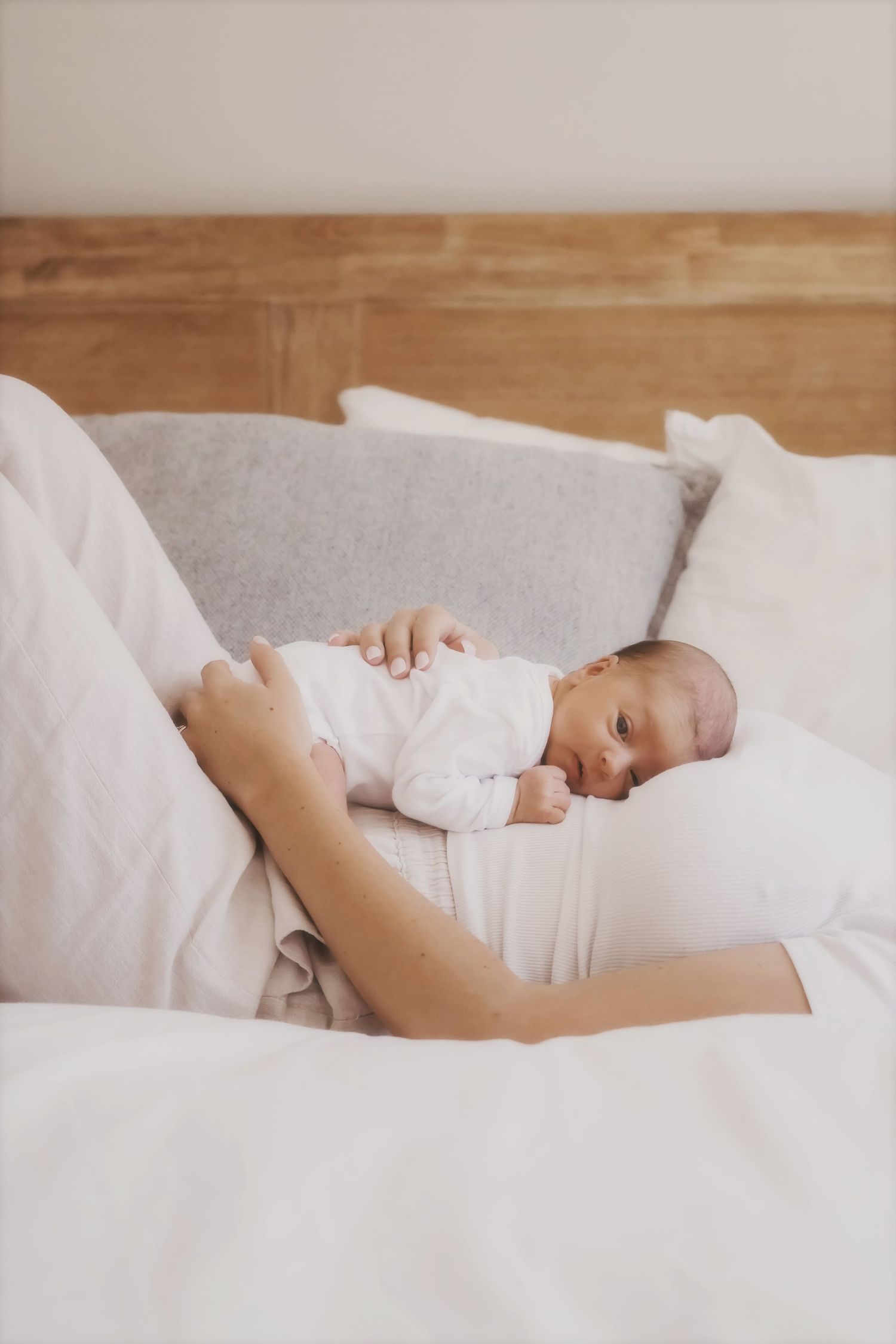 Newborn lying on mum's chest on a white bed, her hand resting gently on their back