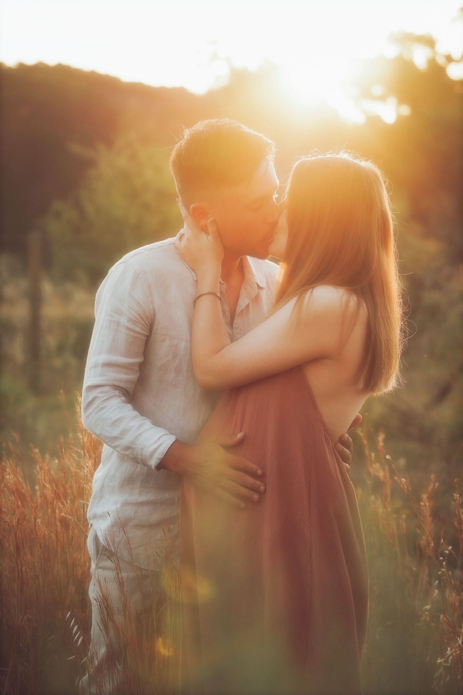 Couple kissing in tall grass, backlit by the golden sun