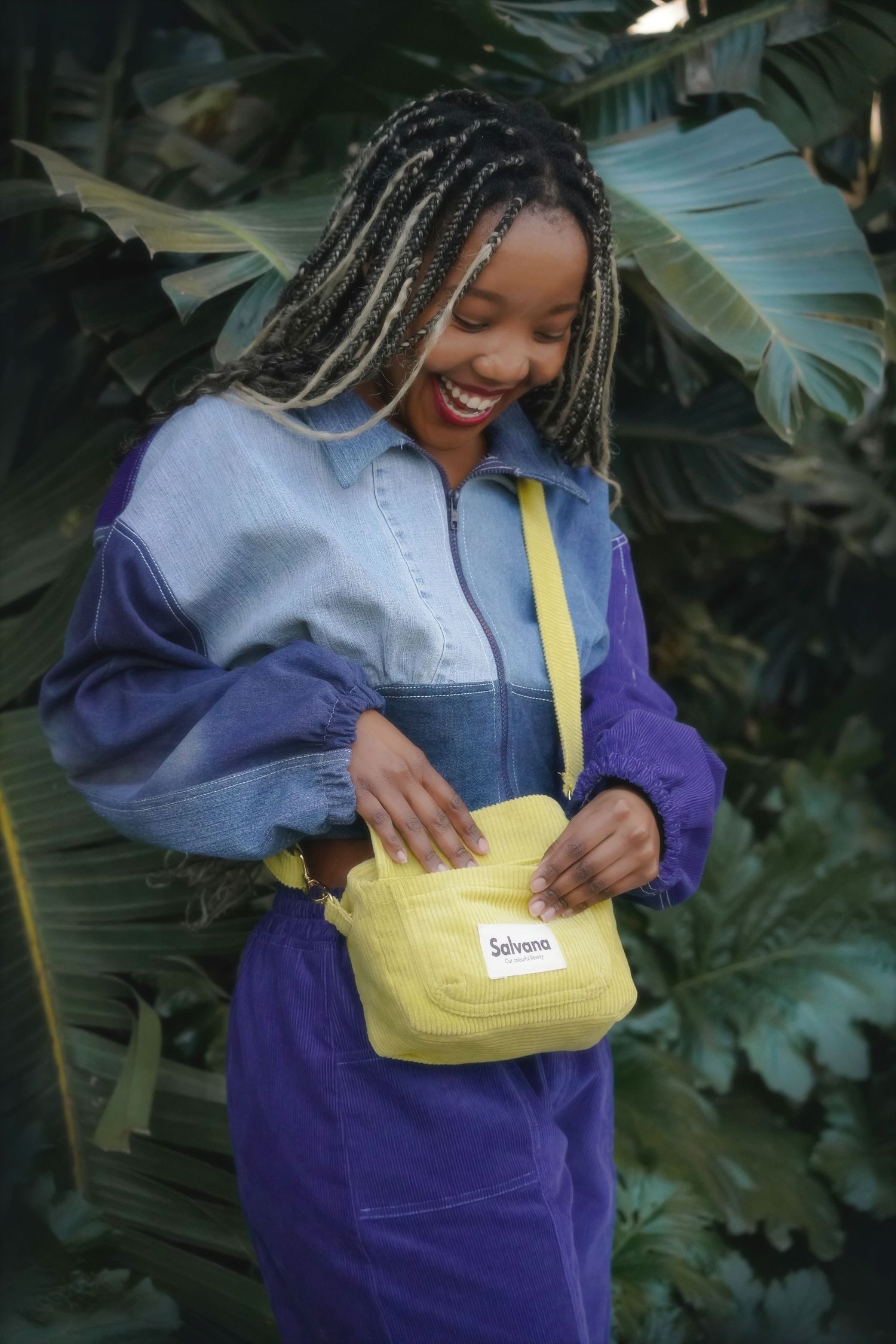 Smiling woman with braids holding a yellow bag, Cape Town brand photoshoot among banana leaves