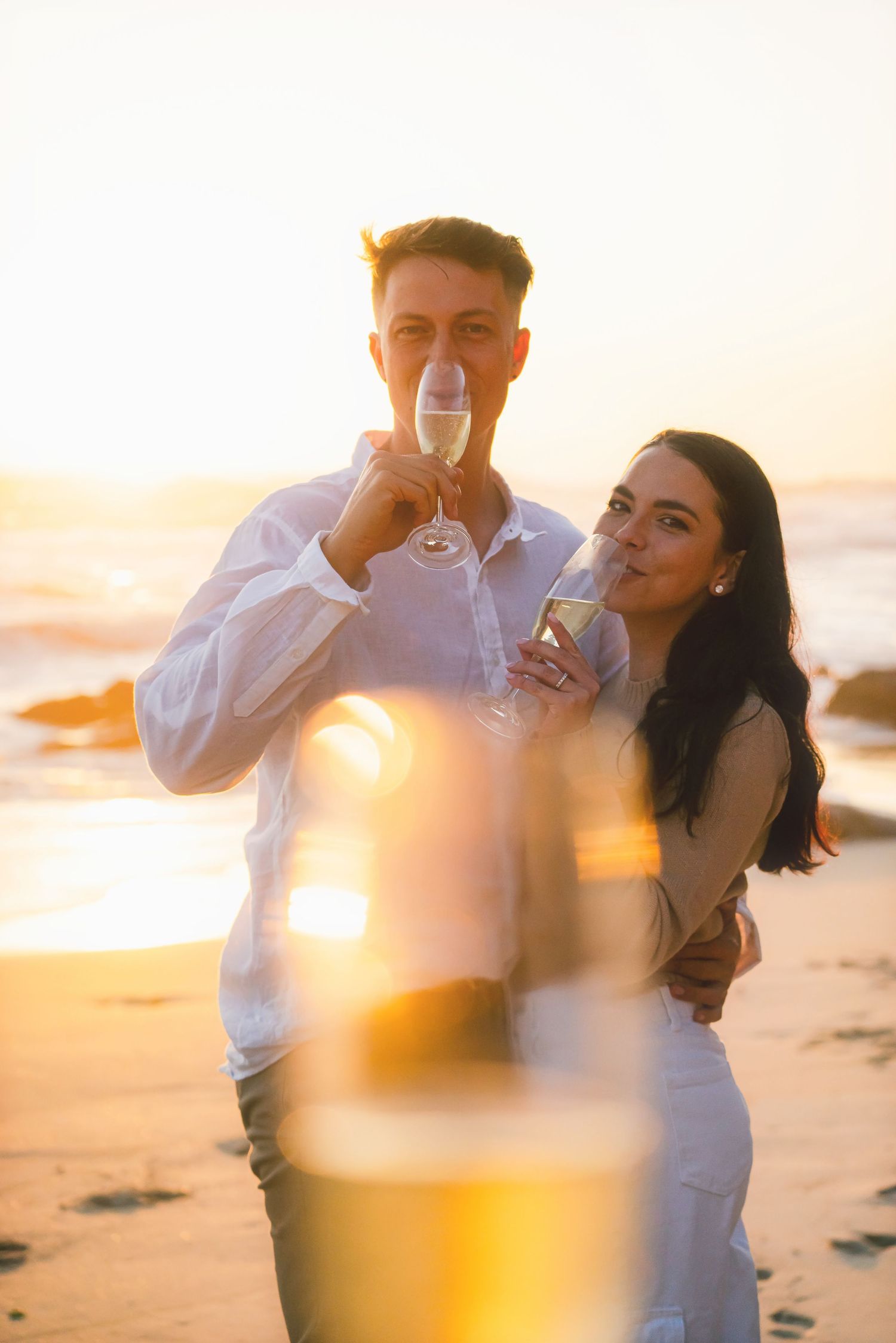 Couple sipping champagne at sunset with a glowing glass blurred in the foreground