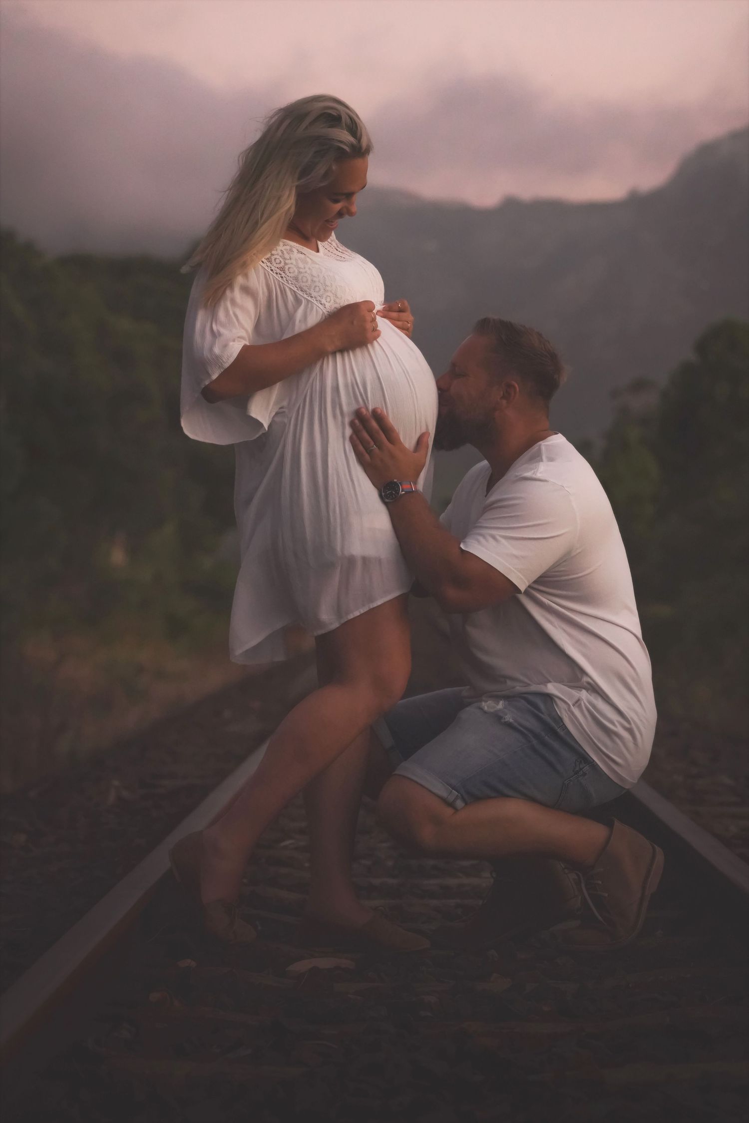 Pregnant woman and man embracing on old railway tracks at dusk