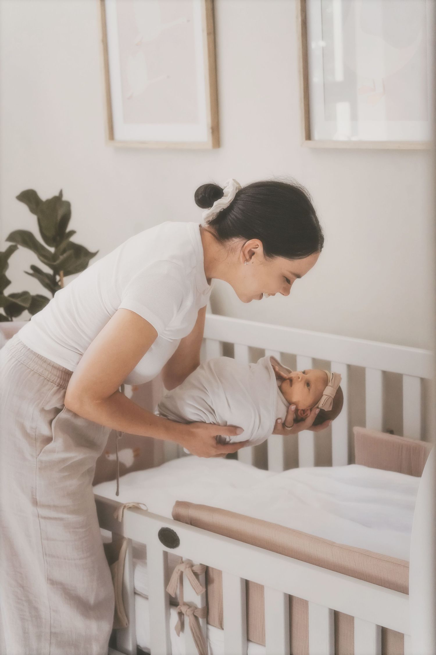 Mother leaning over a white crib to lay her swaddled newborn down
