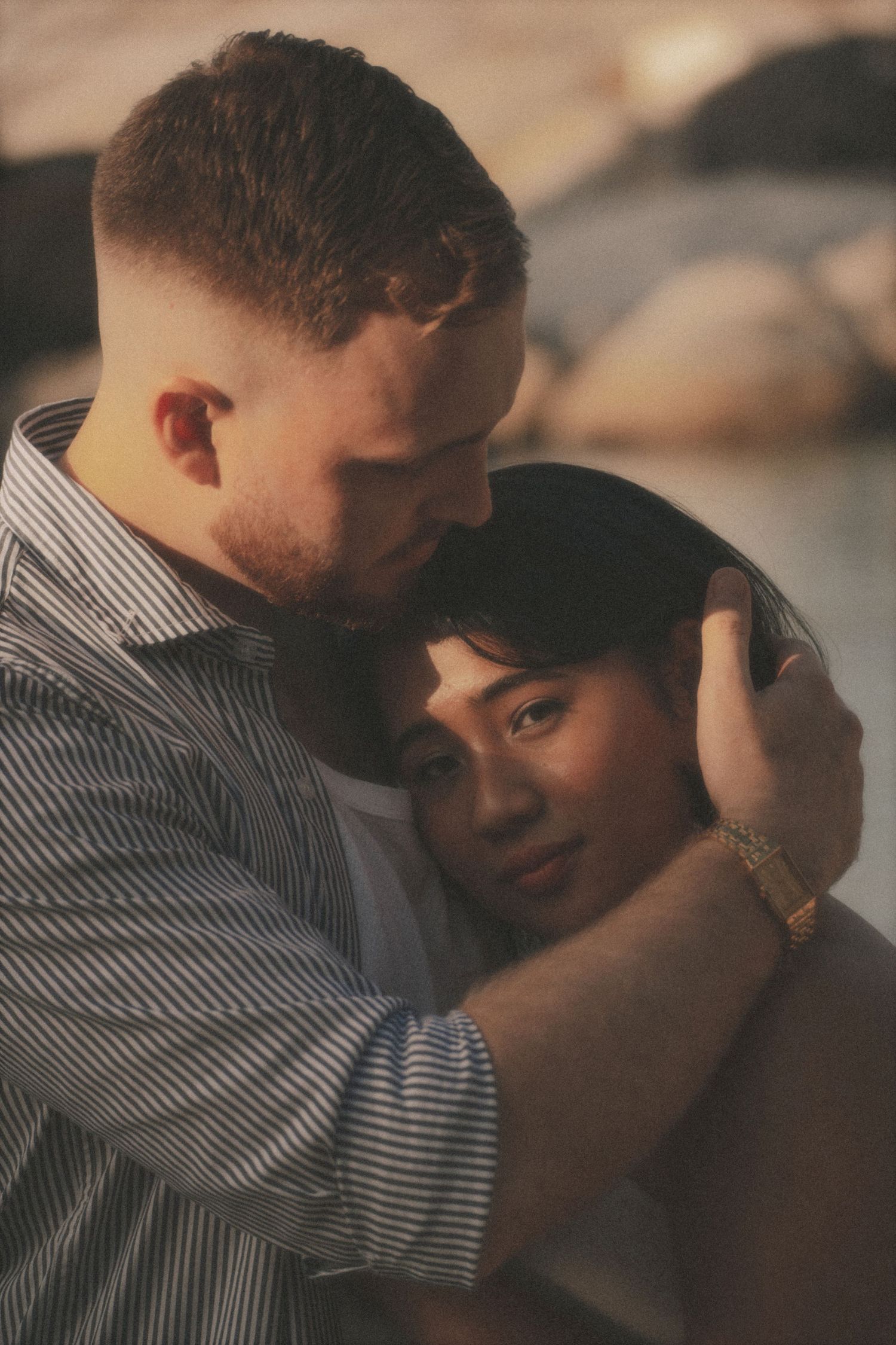 Close portrait of a man holding a woman's head against his chest, rocks softly blurred behind