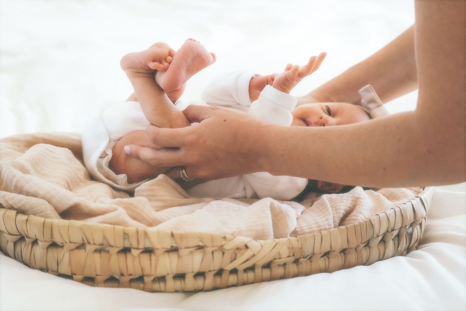 Mother's hands tending to a newborn lying in a woven basket on a beige blanket