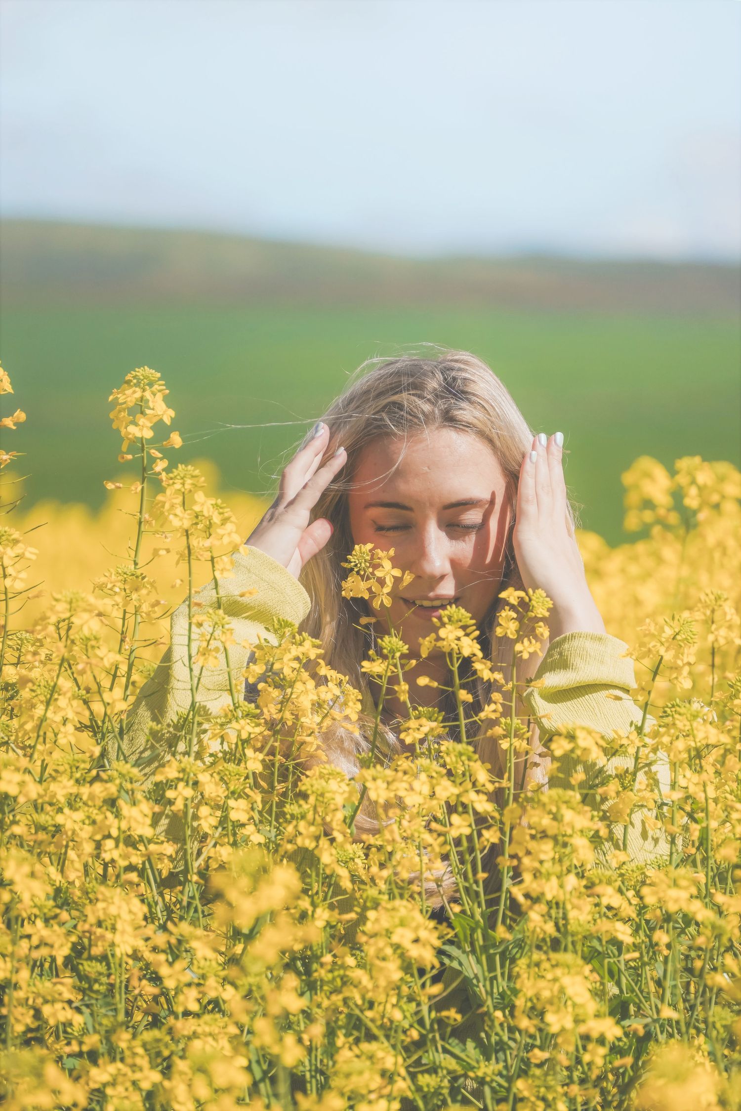 Woman holding her hands to her head among canola, with Cape Town green hills behind