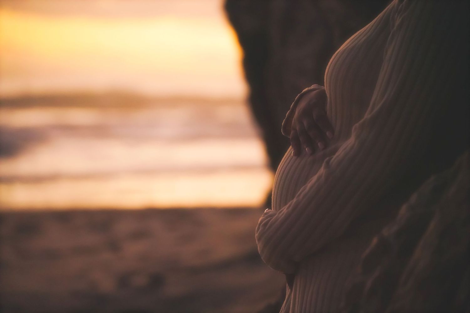 Close-up of a hand on a pregnant belly with sunset glow through a gap in the rocks