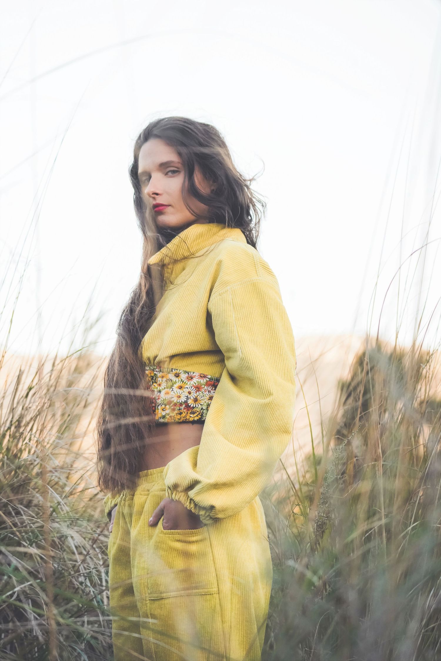 Woman in a yellow corduroy outfit looking over her shoulder in tall grass