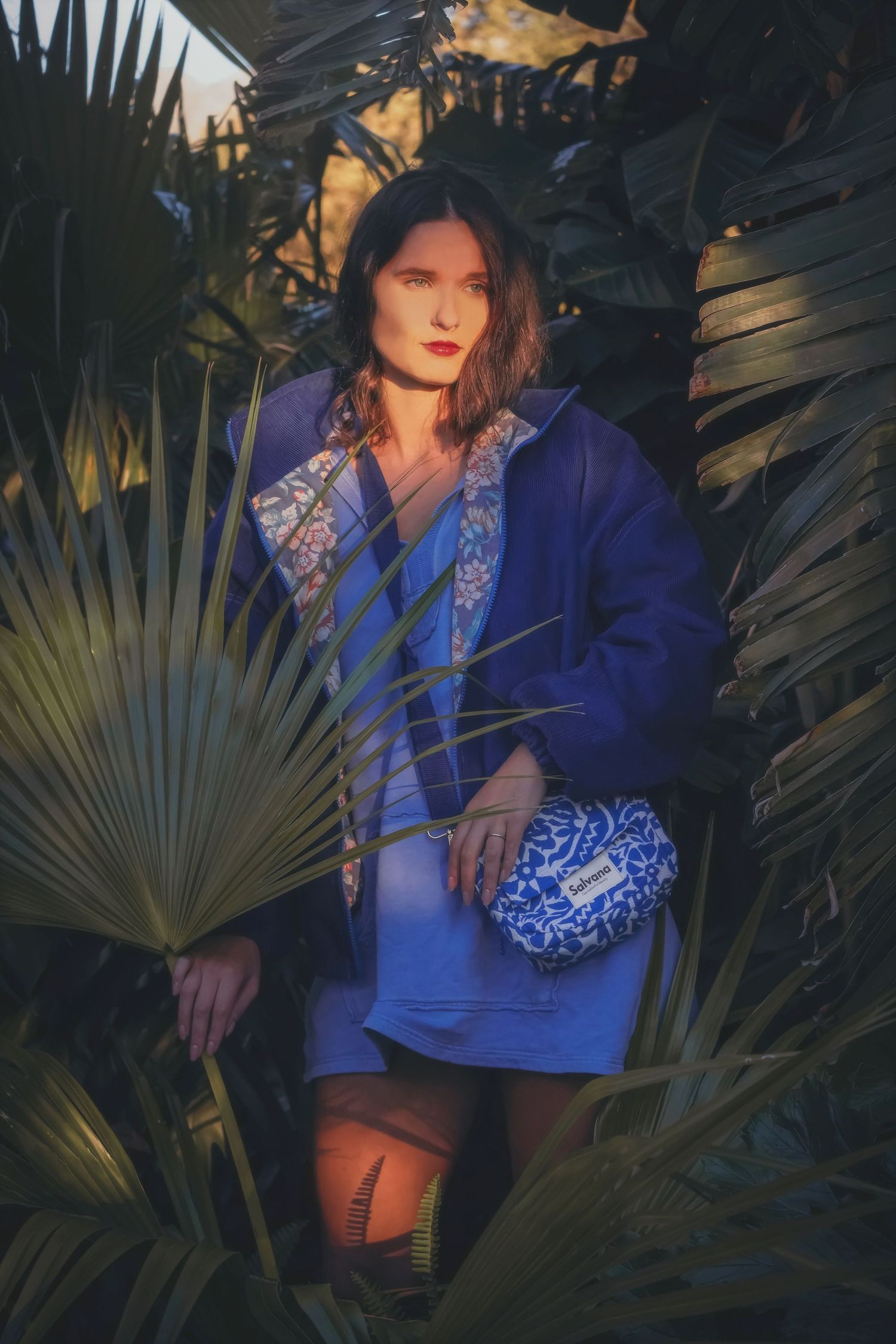 Woman in a blue jacket holding a blue patterned bag among palm fronds in Somerset West