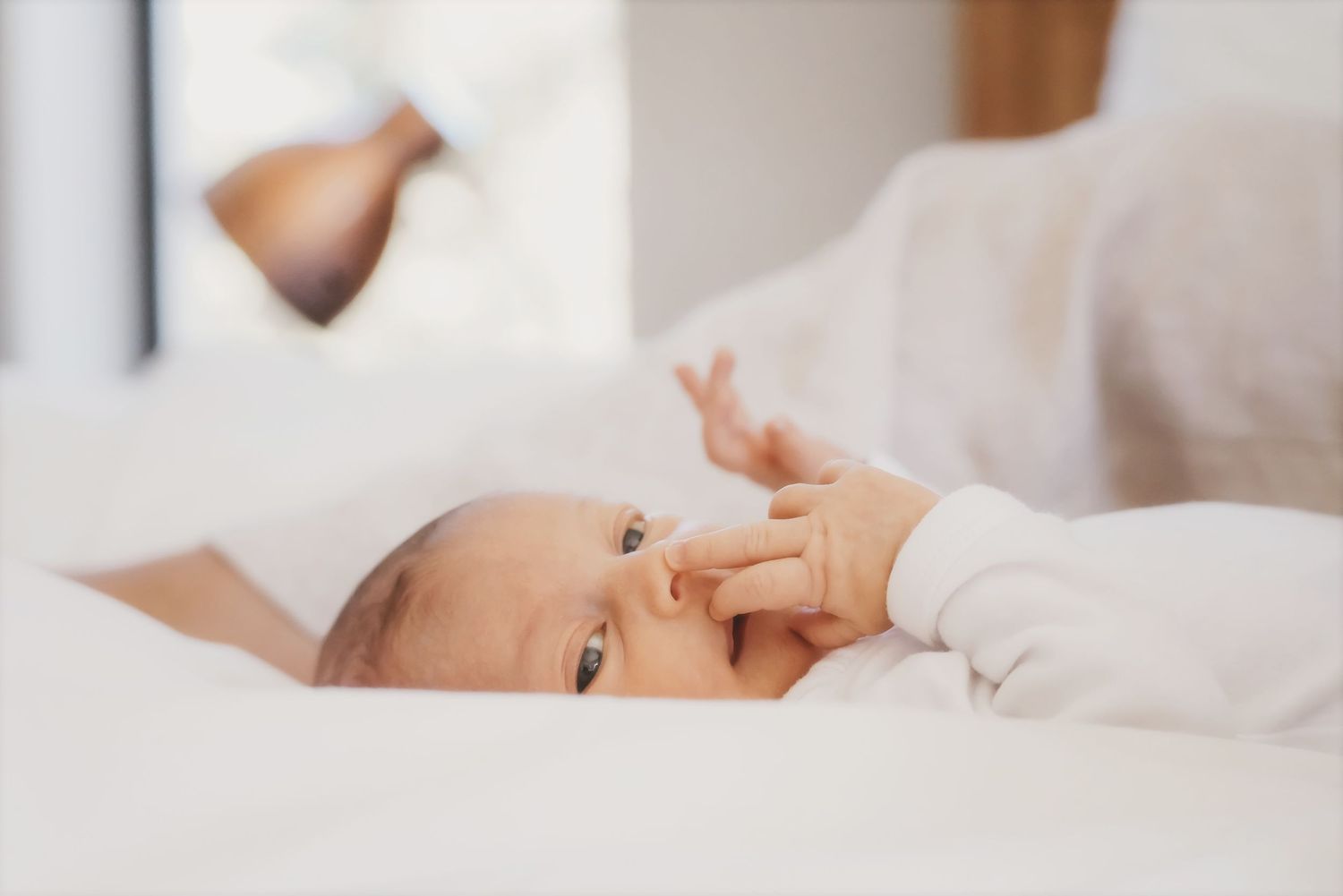 Mother leaning over a newborn lying in a woven basket on the bed, hands gently tending