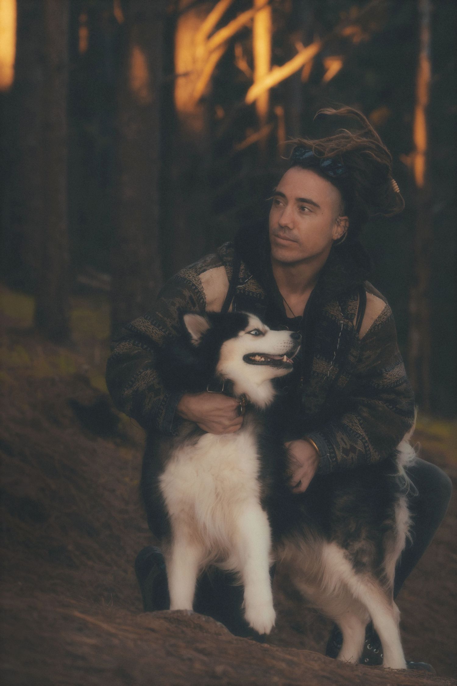 Man crouching in a Cape Town forest, hugging his husky as golden light filters through the trees