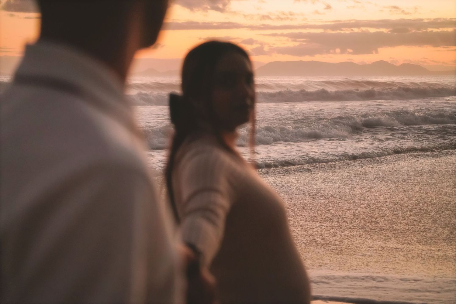 Woman's face softly blurred as she looks back over the sea, her partner's shoulder in the foreground