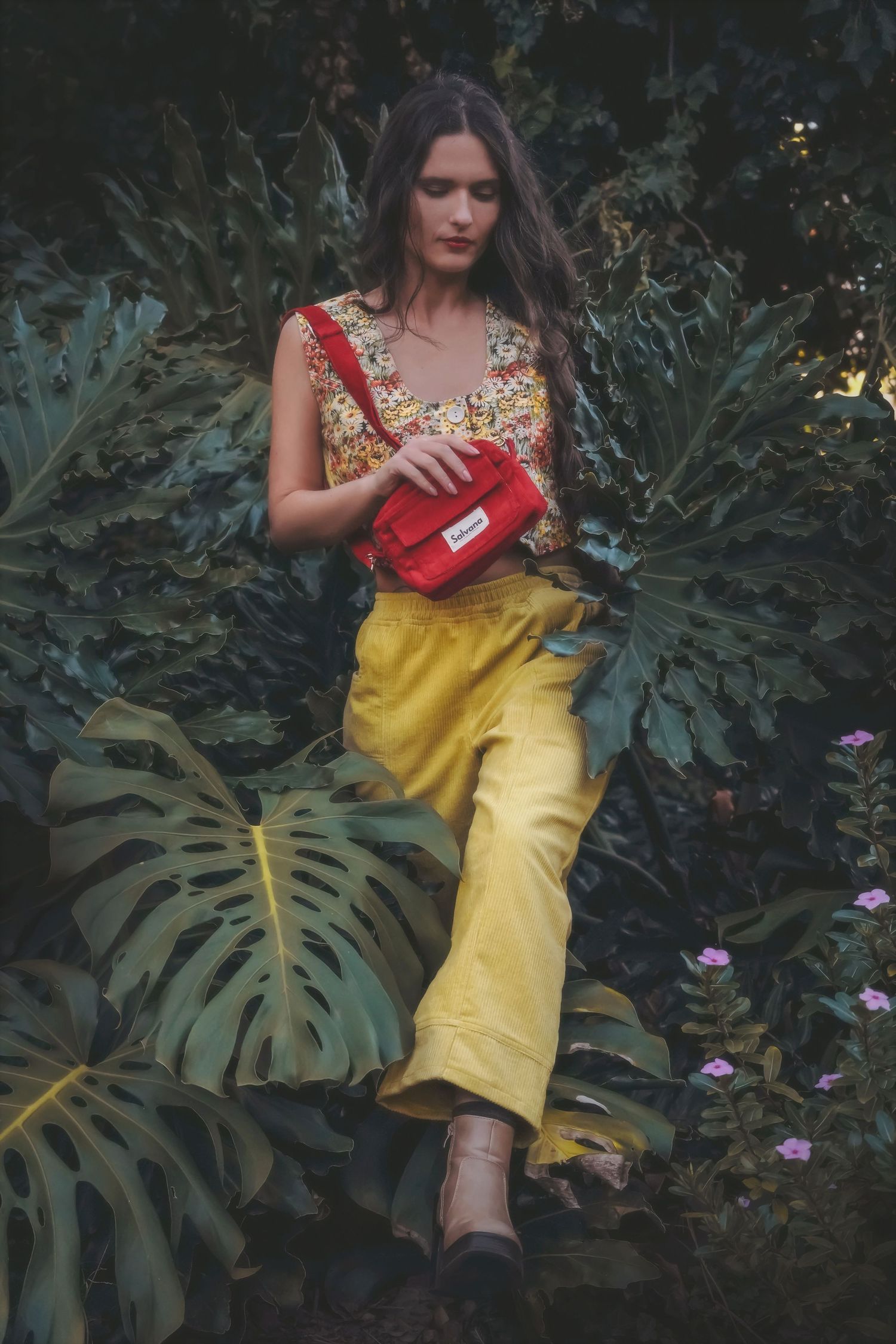 Woman in a floral top and yellow trousers carrying a red belt bag through the jungle foliage
