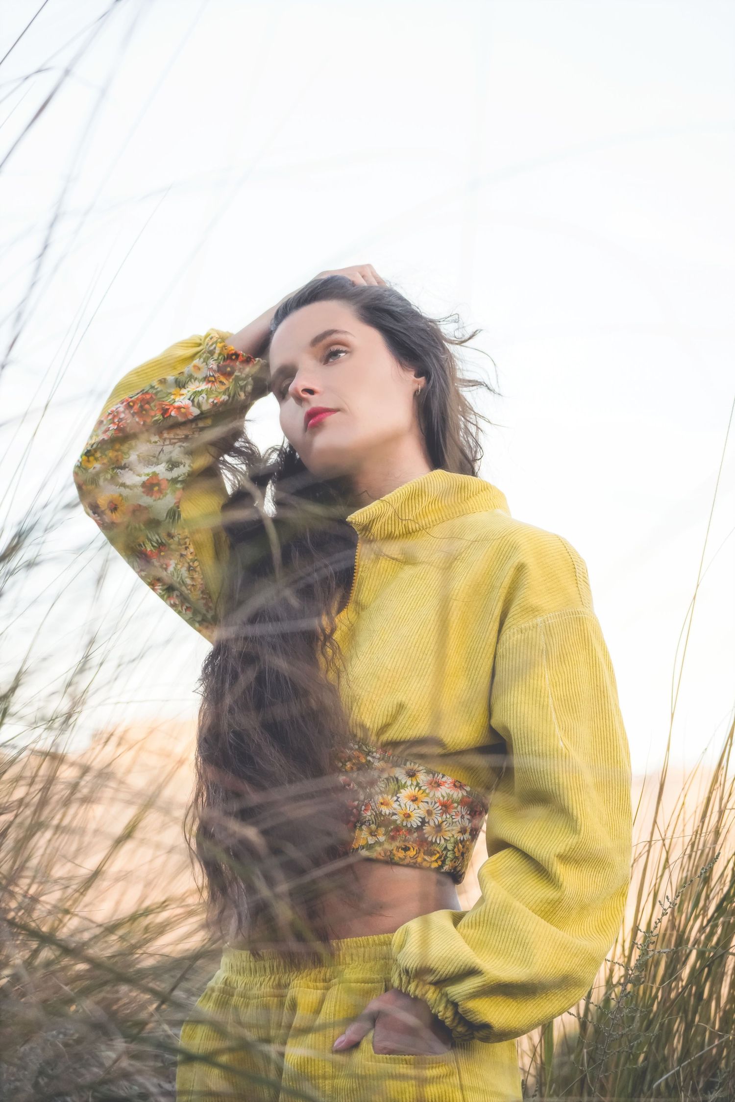 Woman in a yellow corduroy jacket and trousers, one hand in her hair, looking aside