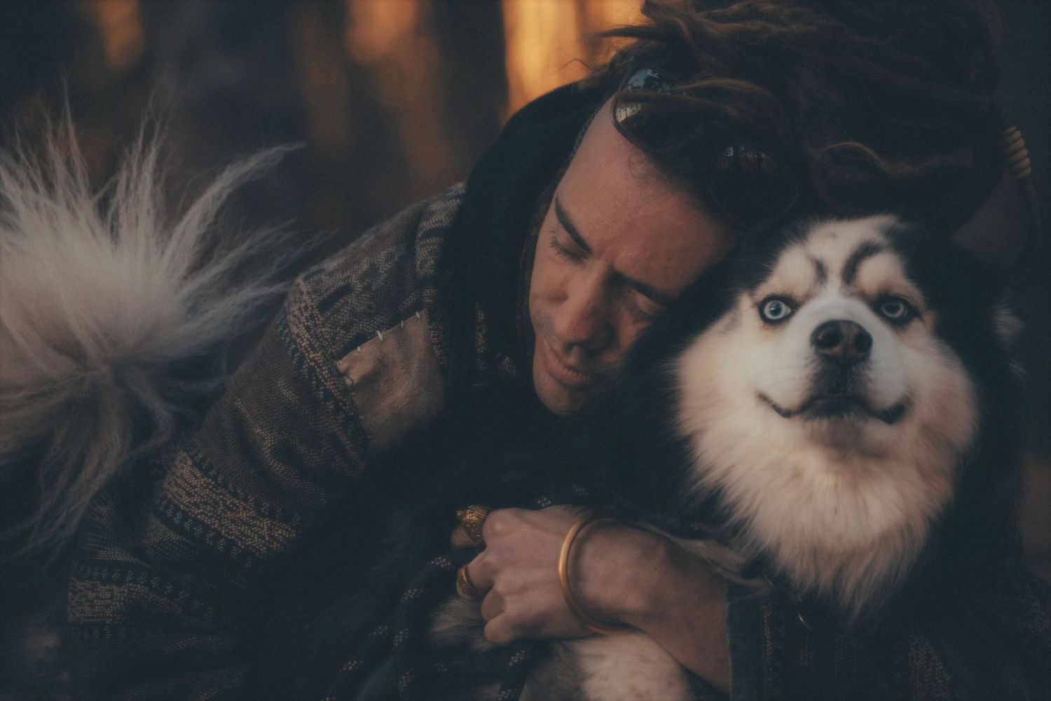 Man resting his cheek against his husky in a moody pine forest