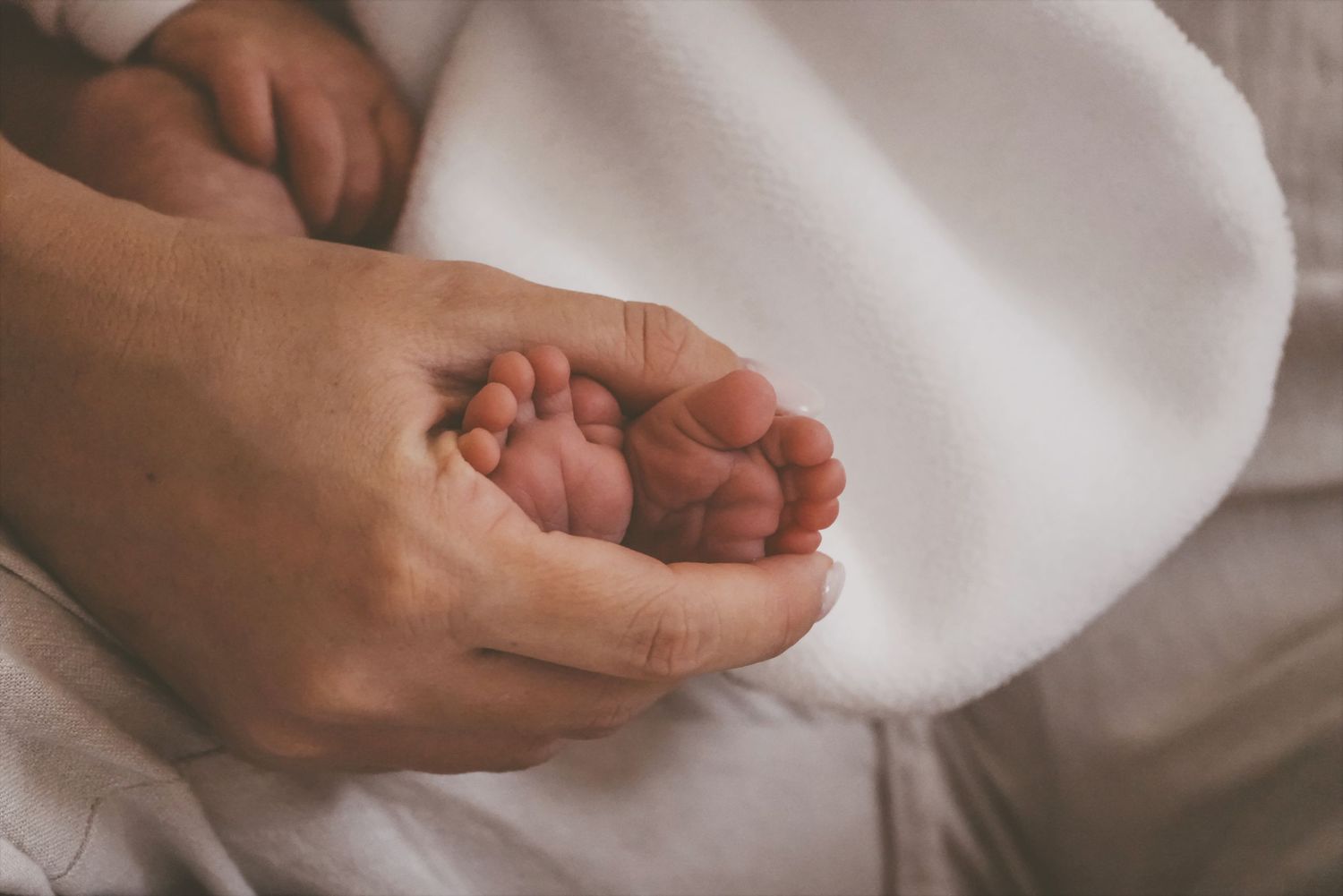 Mother's hands gently cradling a newborn's tiny feet on a soft white blanket